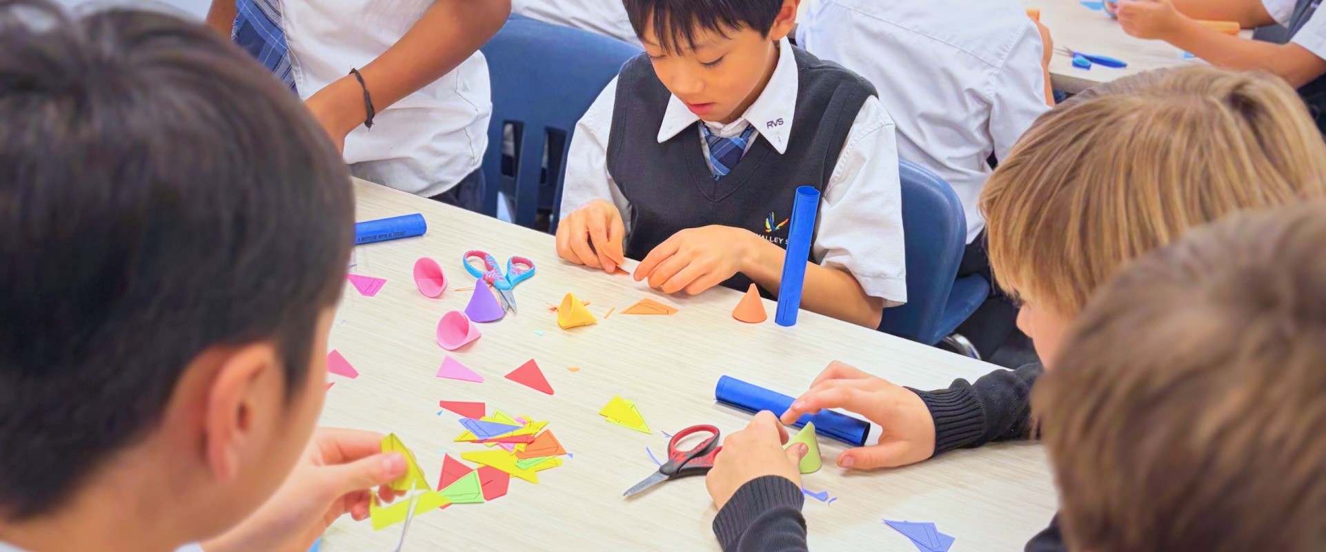 Students cut and fold coloured paper into cones at a shared table.