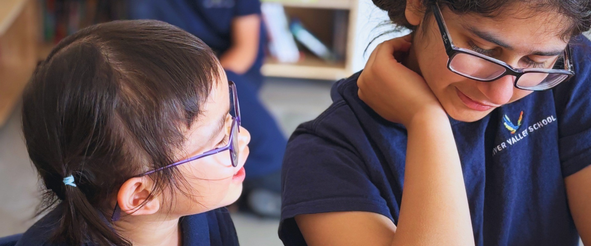 An older student and a younger student smile together during class.