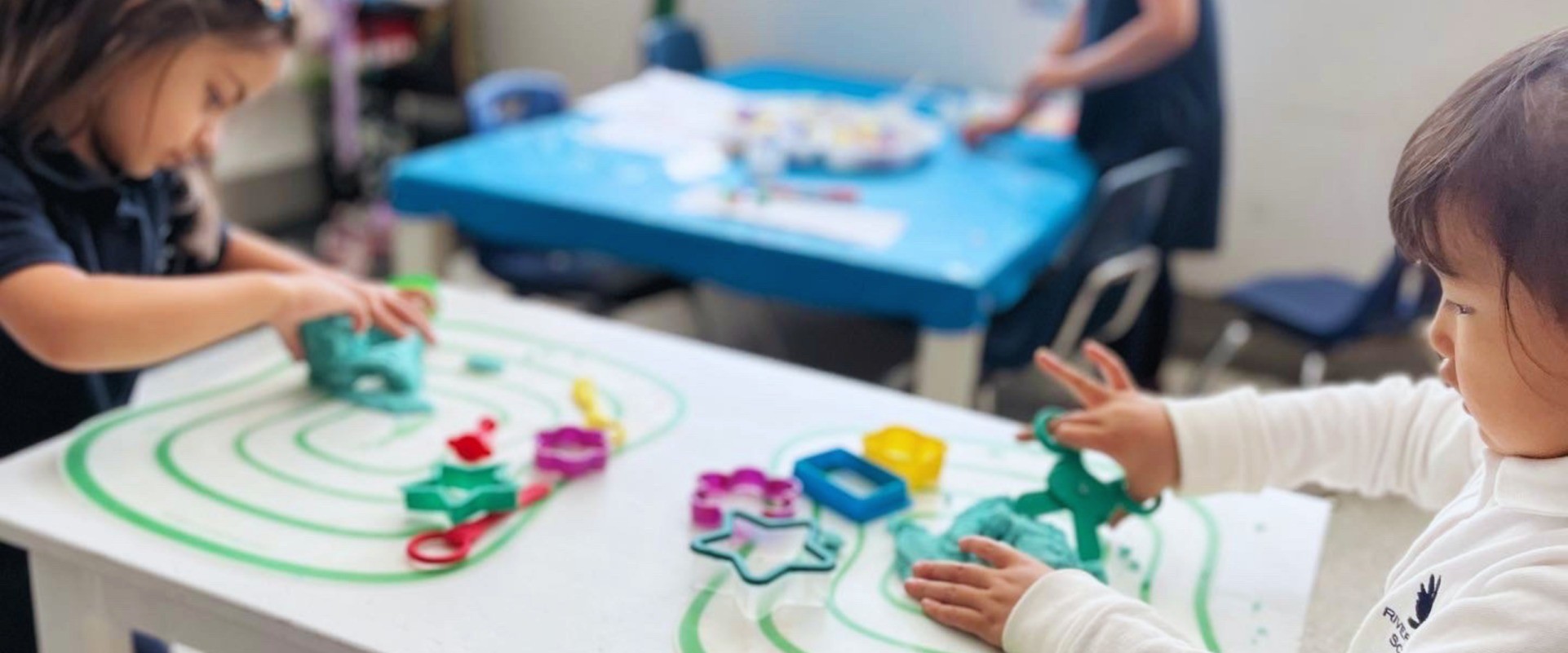 Young students shape play dough with cookie cutters at a classroom table.
